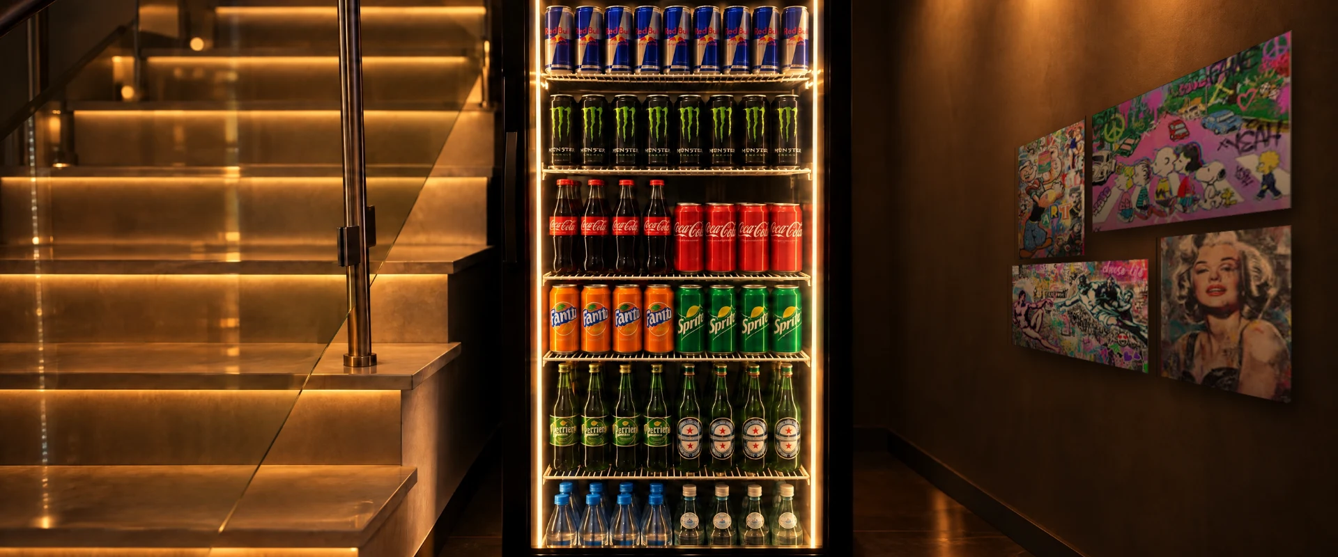Glowing drinks fridge next to the lit staircase, pop-art canvases on the wall